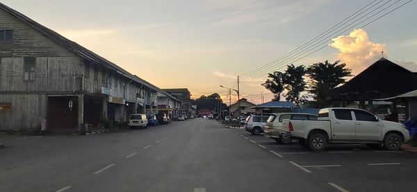 Cars on road by buildings against sky during sunset