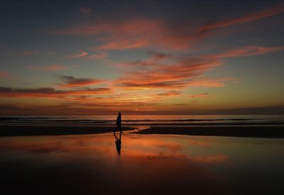 Silhouette person walking at beach against sky during sunset