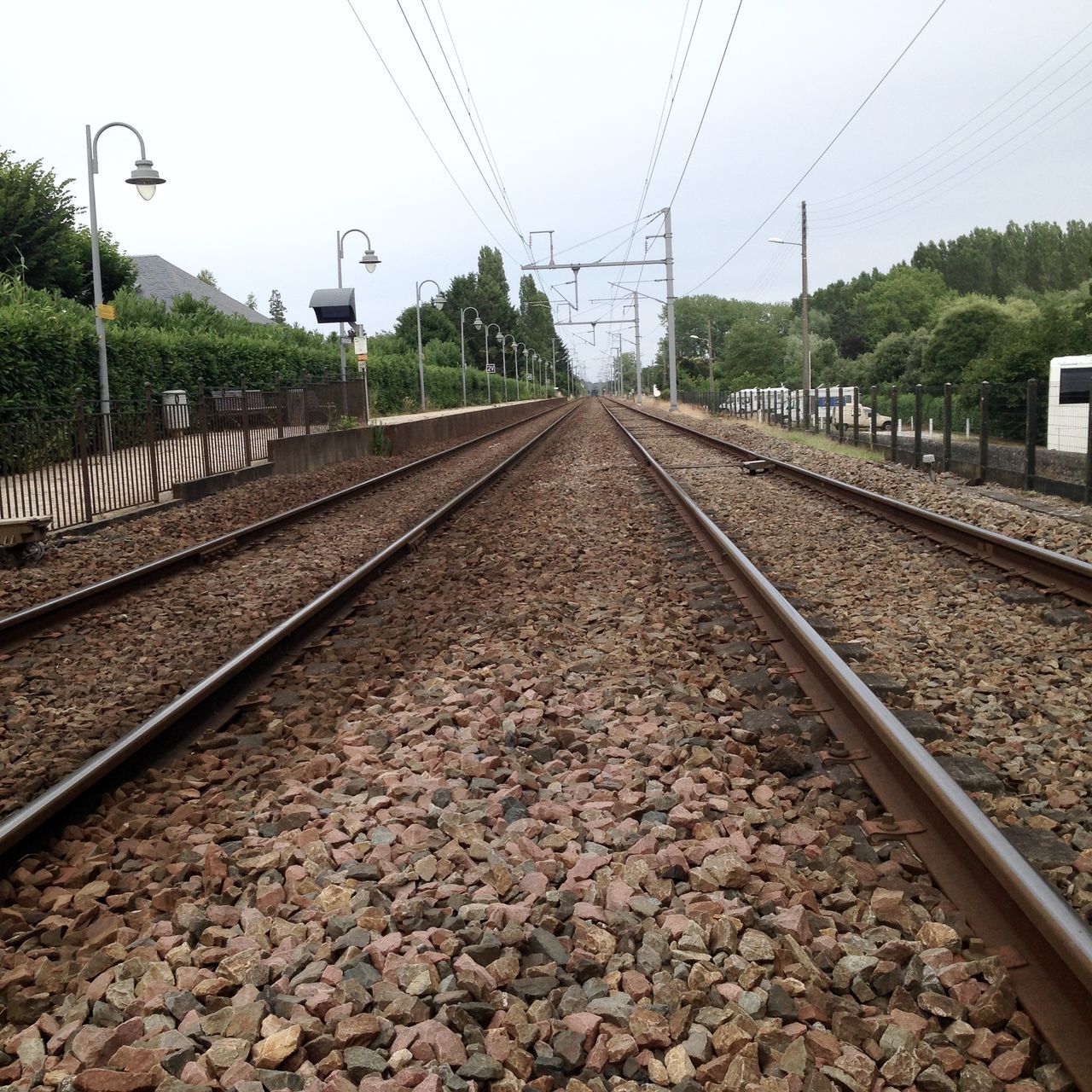 railroad track, rail transportation, transportation, the way forward, power line, diminishing perspective, public transportation, vanishing point, railway track, tree, clear sky, electricity pylon, sky, connection, stone - object, day, power supply, railroad station platform, electricity, gravel