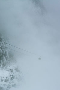 Low angle view of overhead cable car against sky during foggy weather