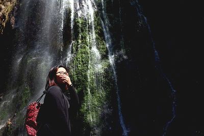 Low angle view of young woman against waterfall