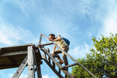 Man climbing on ladder against sky