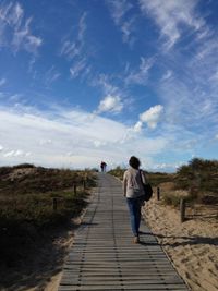 Rear view of man walking on footpath against sky