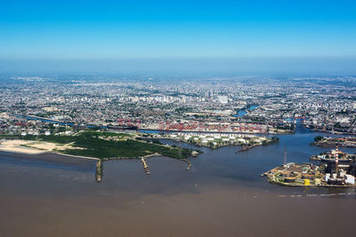 Aerial view of cityscape by sea against clear blue sky