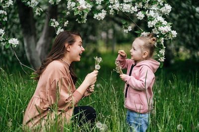 Mother and daughter with dandelions blooming apple trees