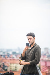 Man using smart phone while standing on terrace against sky