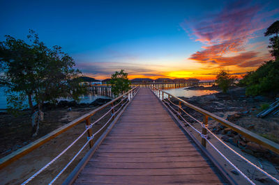 Footbridge amidst trees against sky during sunset