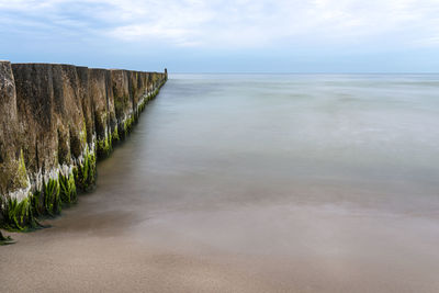 Wooden breakwater covered with moss, arranged in a row at sea, long exposure time, blurred sea waves