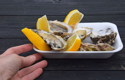 Cropped hand having lemon and oysters at table