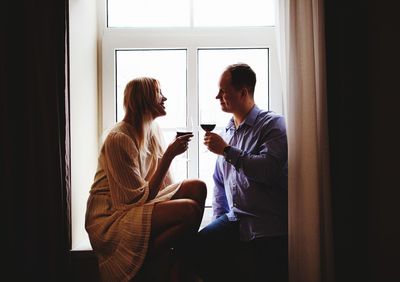 Couple holding drink while sitting by window