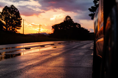 Road by silhouette trees against sky during sunset