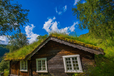 Low angle view of cottage amidst trees and building against sky