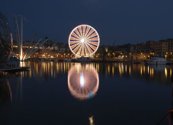 Illuminated ferris wheel by lake against sky in city at night