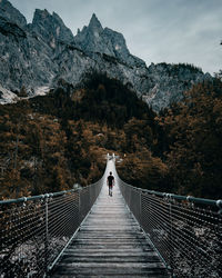Rear view of man walking on footbridge leading towards mountain