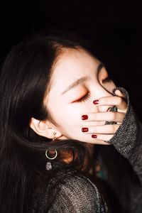 Woman covering mouth with hand against black background