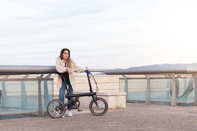 Young woman leaning on electric bike  waiting for her friend in a city park at the afternoon