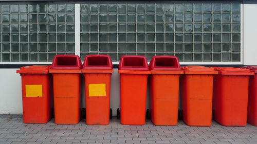 Orange colour garbage bins in a row against wall 