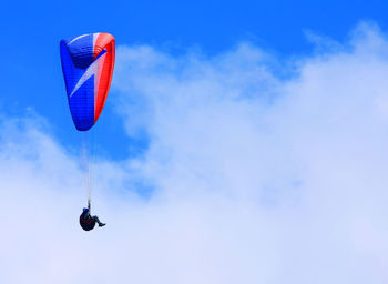 Low angle view of man paragliding in cloudy sky