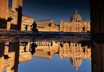 Reflection of buildings in puddle on footpath against sky