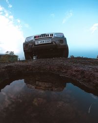 Reflection of abandoned car on water against sky