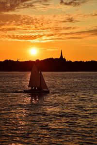 Silhouette sailboat in sea against sky during sunset