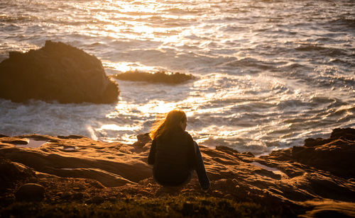 Rear view of woman sitting on rock at beach