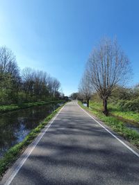 Empty road amidst trees against sky