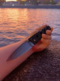 Midsection of woman holding umbrella at sea during sunset