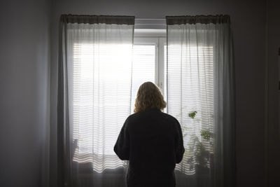 Rear view of teenage girl looking through window