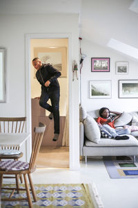 Mother using mobile phone on sofa while boy in storage room at home