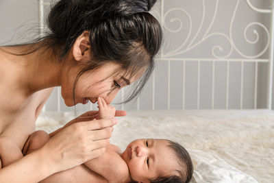 Close-up of shirtless woman holding naked newborn son on bed at home