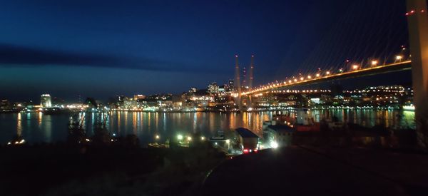 Illuminated city by river against sky at night