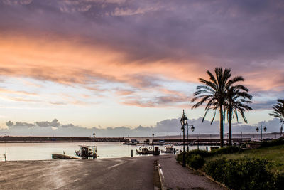 Road by sea against sky at sunset