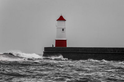 Lighthouse by sea against clear sky