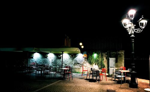 Empty chairs and table against illuminated street light at night