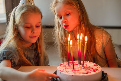 Little twin girls, children blow out candles cake birthday party at home. holiday during quarantine