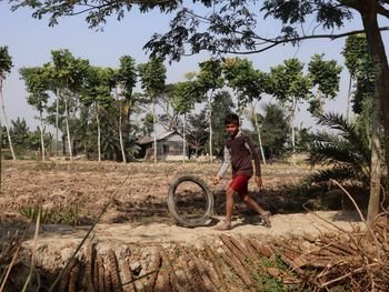 Boy hitting motorcycle tyre on dirt road against sky.