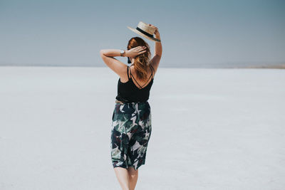 Rear view of young woman standing on field against sky