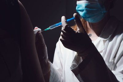 Midsection of doctor wearing mask vaccinating person on hand