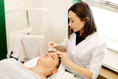 A cosmetologist massages the skin of a young woman with a gouache scraper. facial massage, skin care