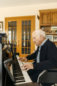 Senior man sitting in wheelchair playing piano at home