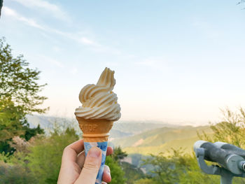 Hand holding ice cream cone against sky