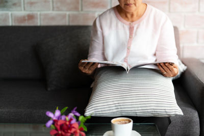 Old woman reading a book with cup of coffee at home