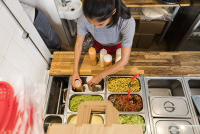 High angle view of young female chef arranging sauce bottles in container at commercial kitchen