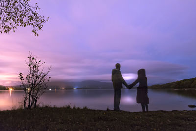 Digital composite image of friends standing against lake during sunset