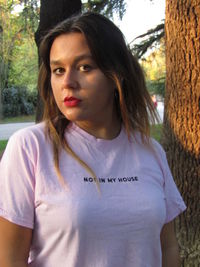 Portrait of beautiful young woman standing by tree trunk