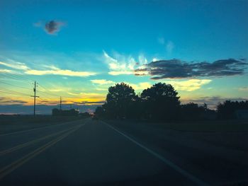 Road by silhouette trees against sky at sunset