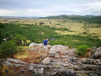 Rear view of man sitting on cliff against landscape