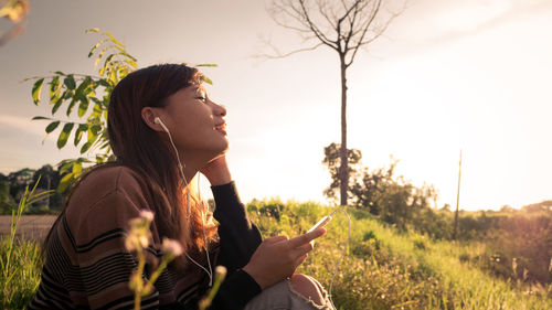 Side view of young woman looking at camera against sky