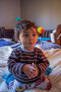 Portrait of cute girl sitting on bed at home